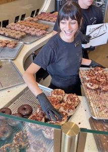 Happy employee serves fresh maple bacon donuts at Sidecar Donuts in Del Mar